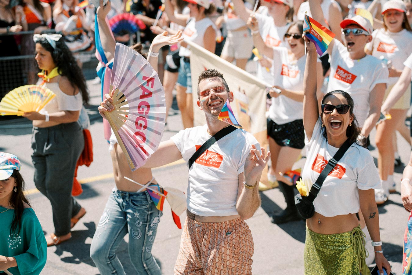 Participants joyfully celebrate at a pride parade, waving rainbow flags and fans.