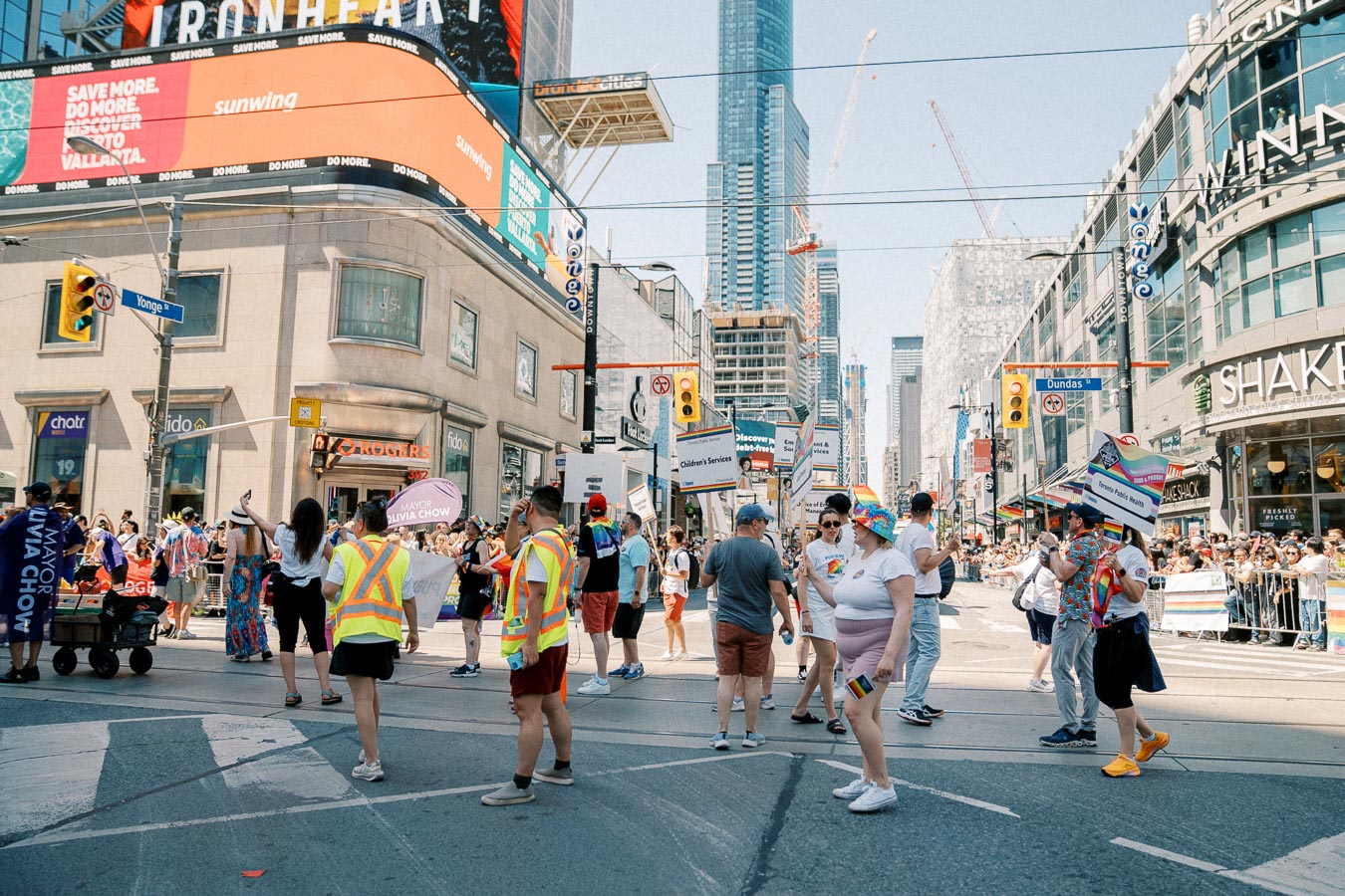 A vibrant parade in Toronto, showcasing participants with rainbow flags and colorful outfits, set against the backdrop of the city's skyscrapers and bustling streets.