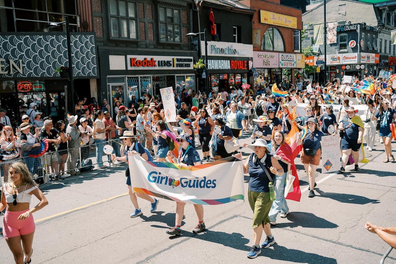 Participants in a parade march under a Girl Guides banner, celebrating diversity and inclusion on a bustling city street.