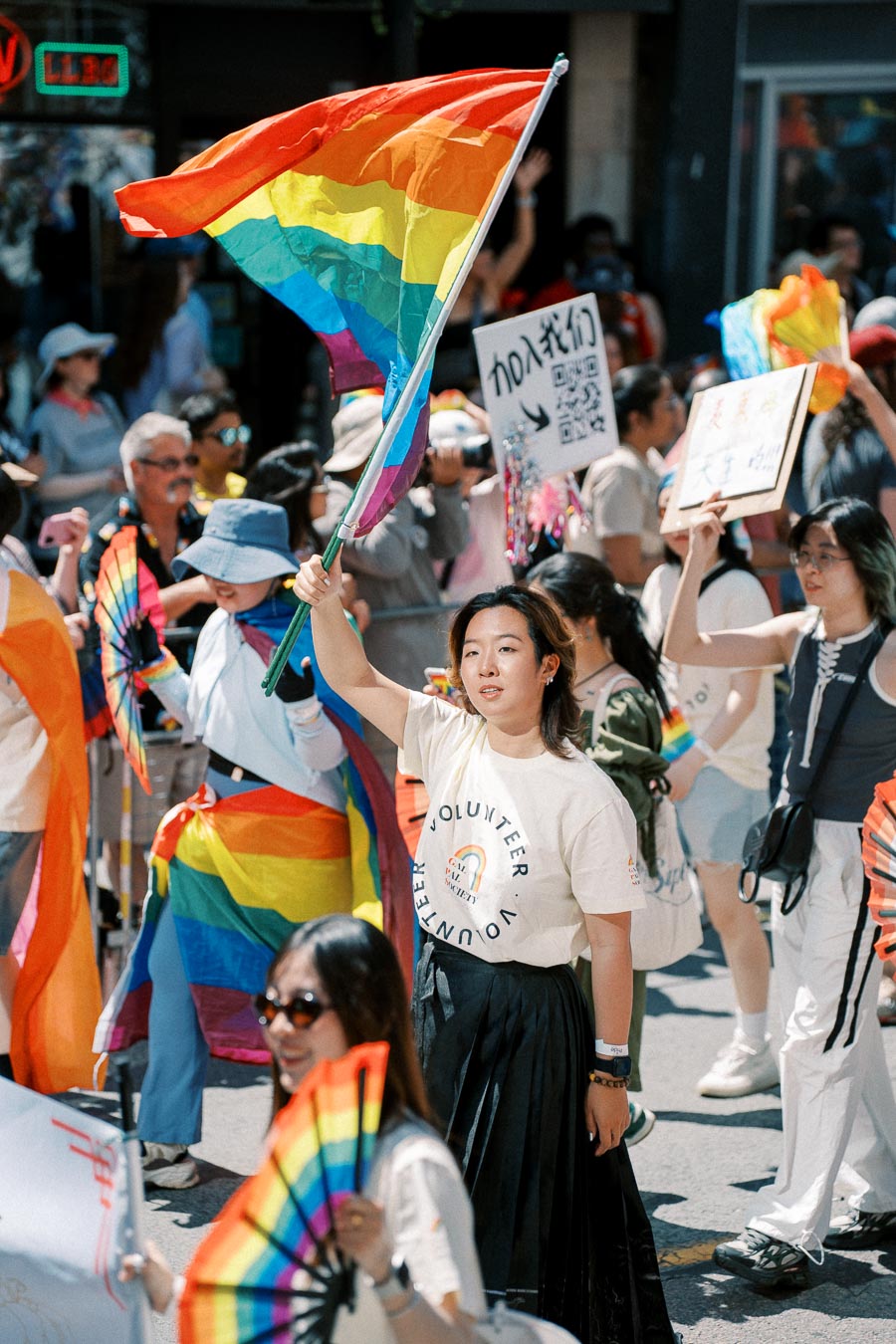 Participants at a pride parade wave rainbow flags and carry signs, celebrating diversity and inclusion.
