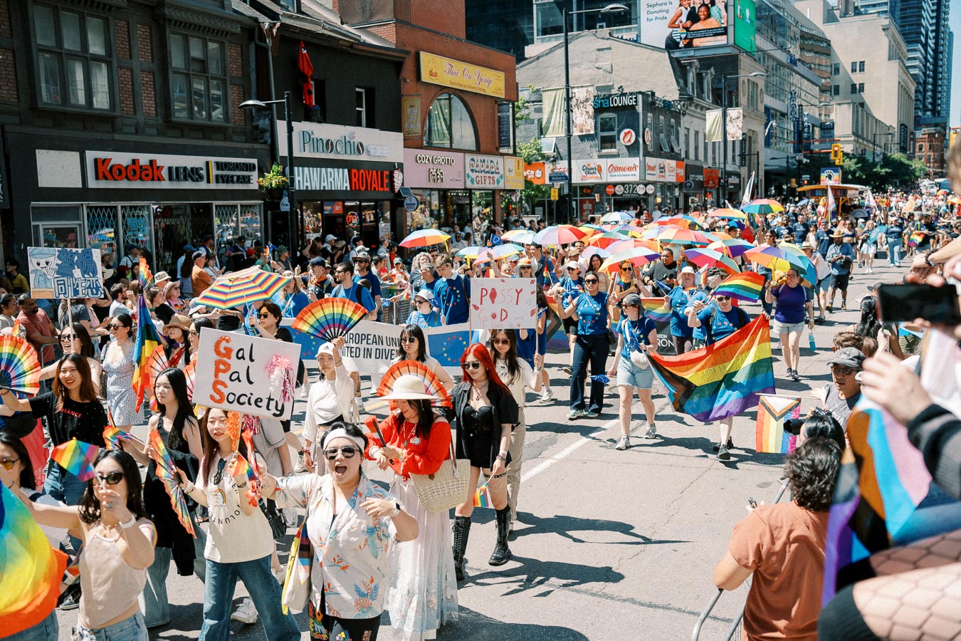 Participants in a lively pride parade march down a city street, showcasing rainbow flags and umbrellas, celebrating diversity and inclusion.