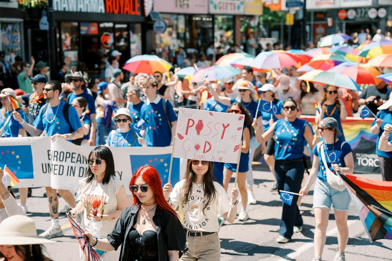 Participants in a pride parade march with rainbow umbrellas and flags, promoting diversity and unity.