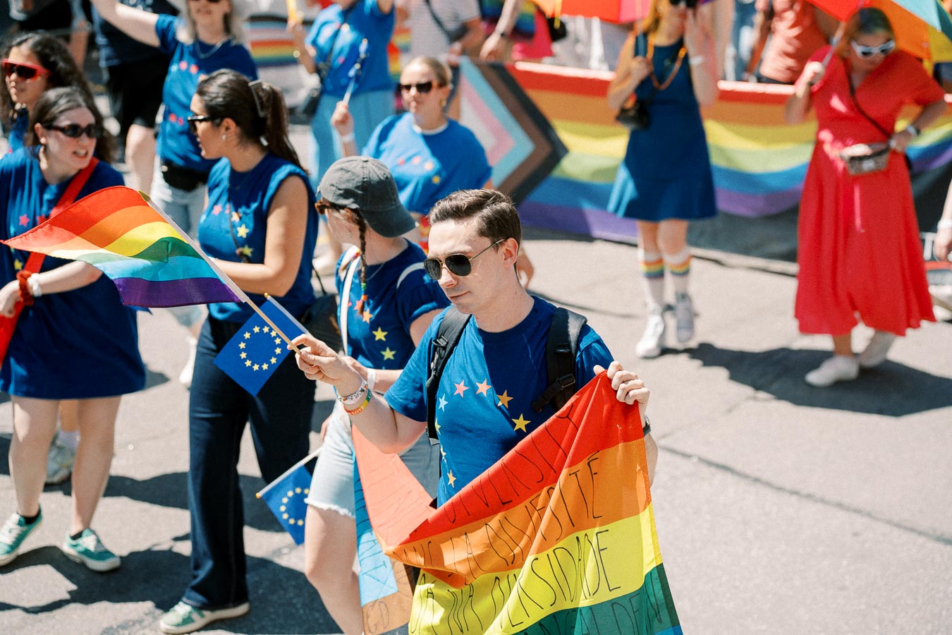 Participants in a pride parade hold rainbow and European Union flags, celebrating diversity and inclusion.