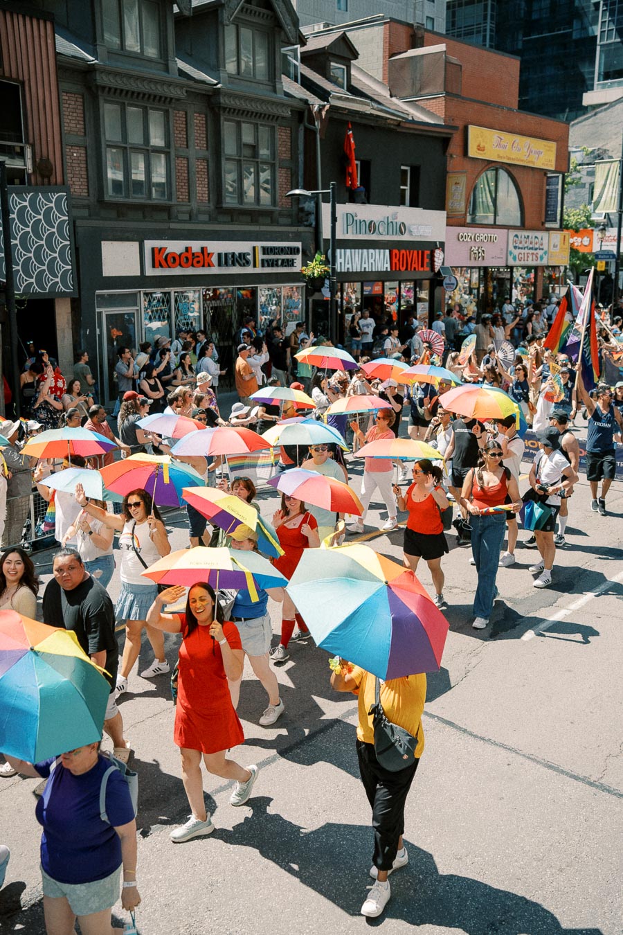 Participants in a lively street parade hold colorful rainbow umbrellas, celebrating diversity and inclusion.