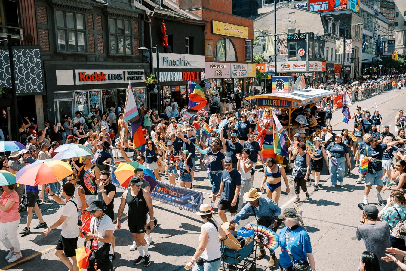 A lively parade scene featuring participants with rainbow flags and umbrellas, celebrating diversity and inclusion on a bustling city street.