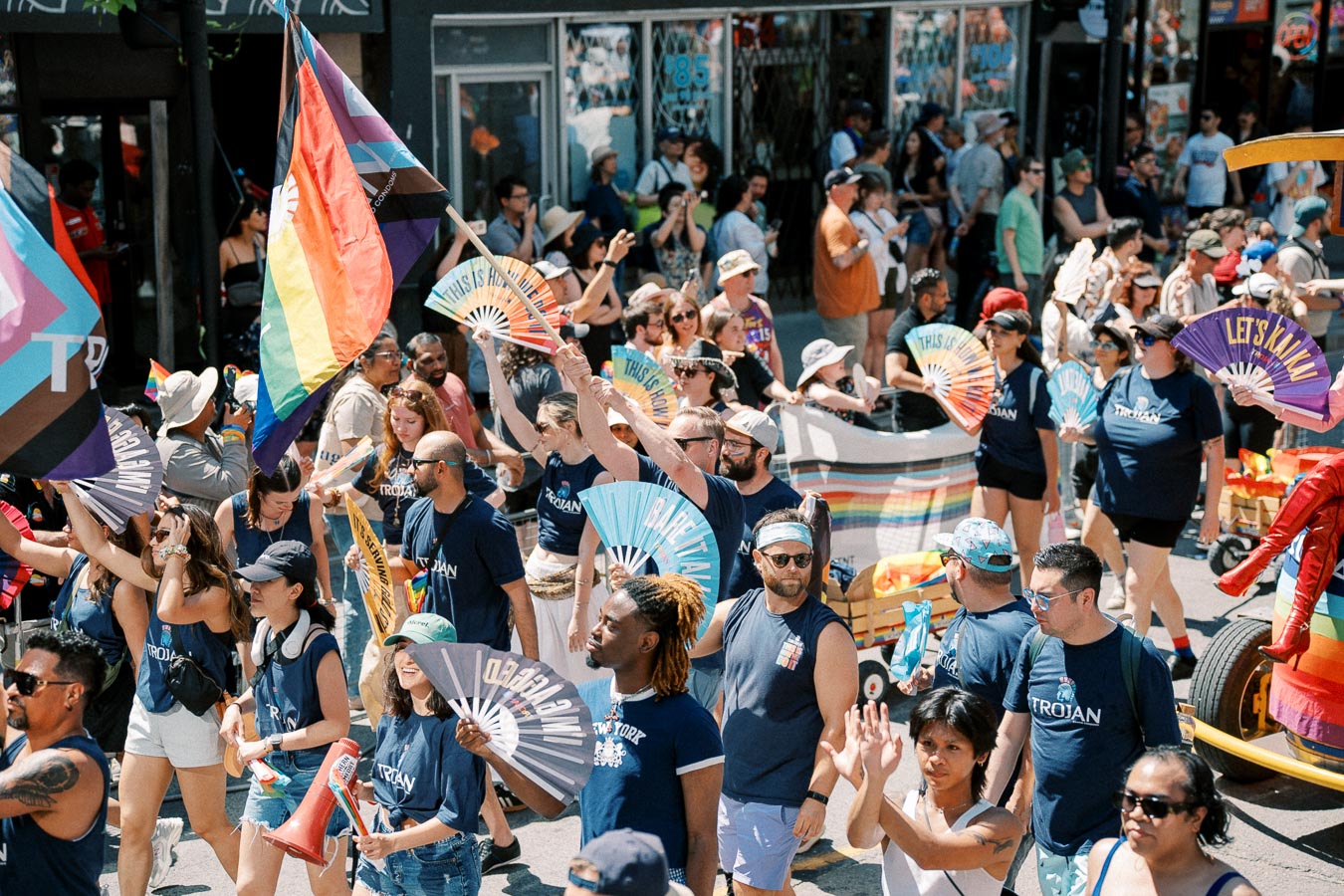 Participants in a vibrant parade celebrate diversity and inclusion, waving rainbow flags and fans.