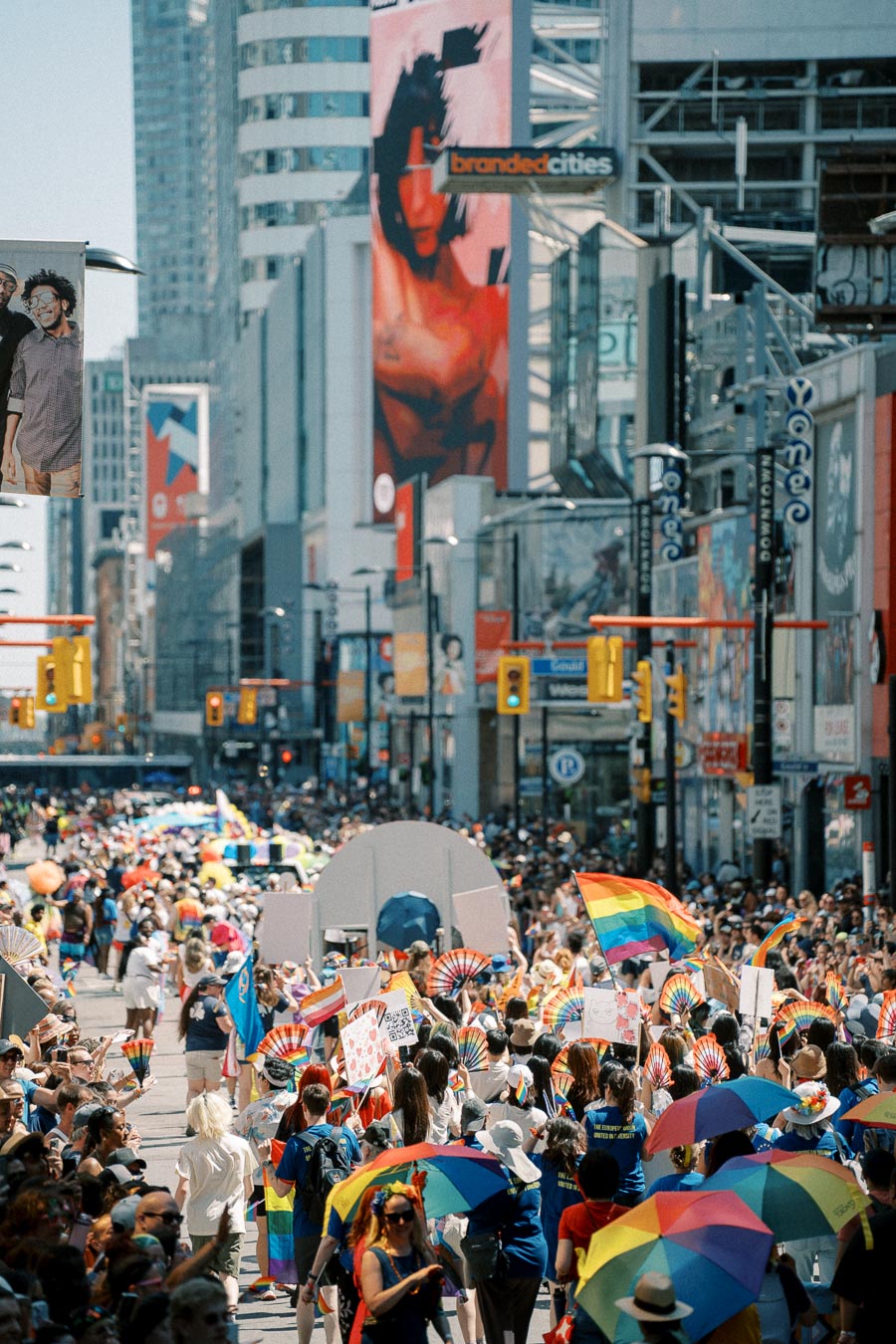 A lively pride parade fills a bustling city street, adorned with rainbow flags and a diverse crowd celebrating.