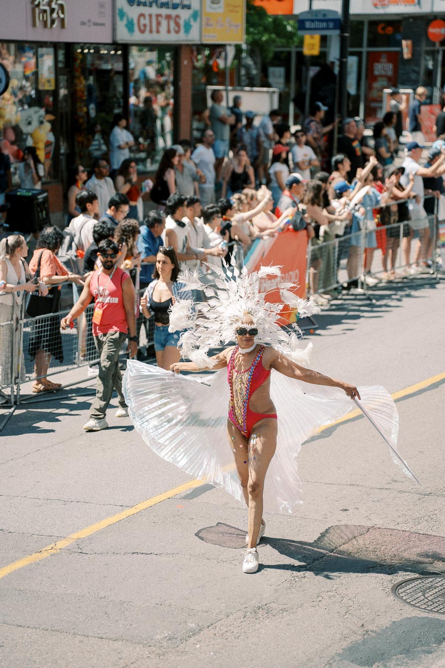 A parade participant in a colorful costume with feathers and a cape entertains the crowd during a street festival.