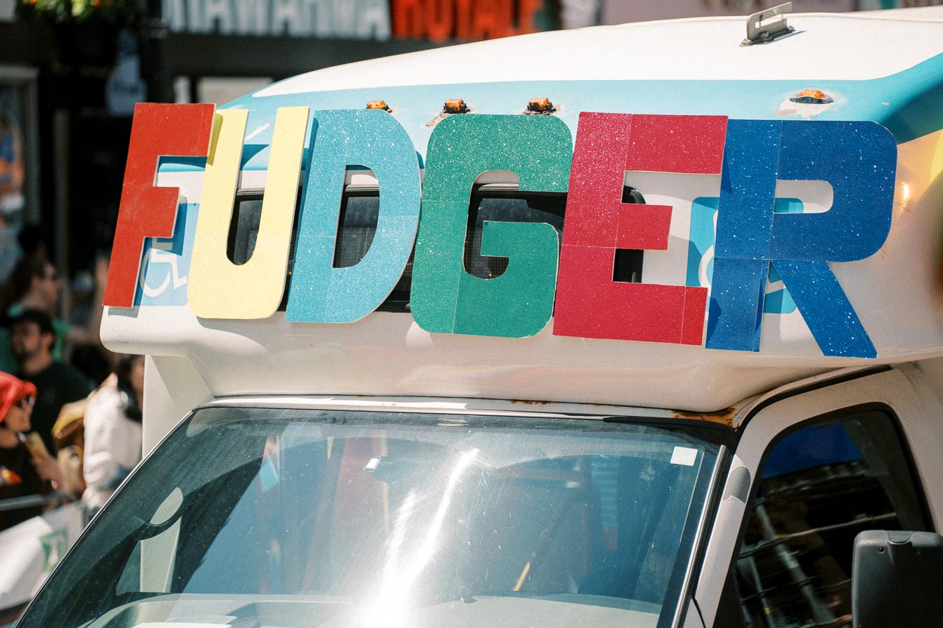 A vehicle with colorful letters spelling 'FUDGER' on the front, likely part of a parade or event.