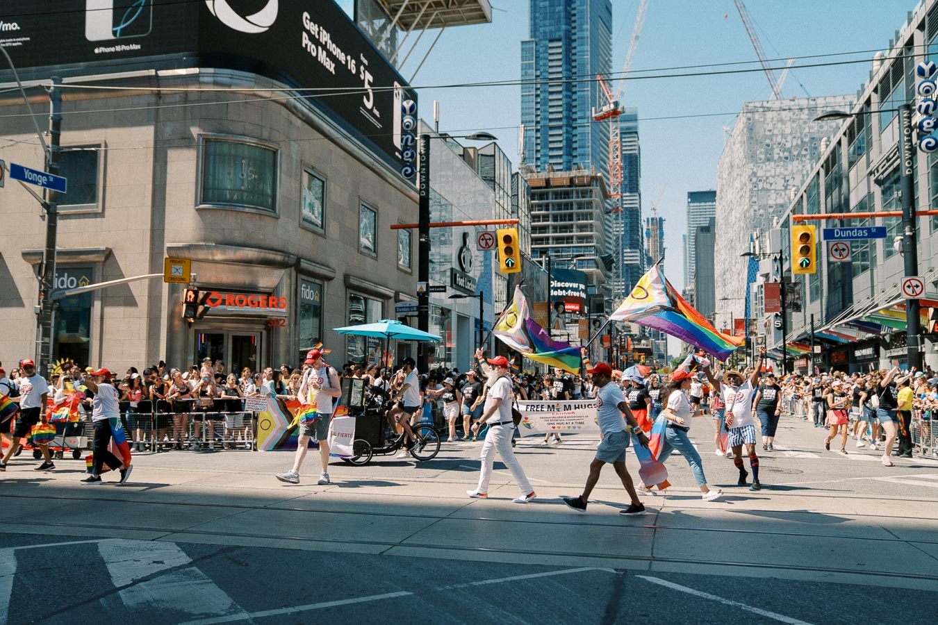 A lively parade featuring participants with rainbow flags, celebrating diversity in a bustling city intersection.