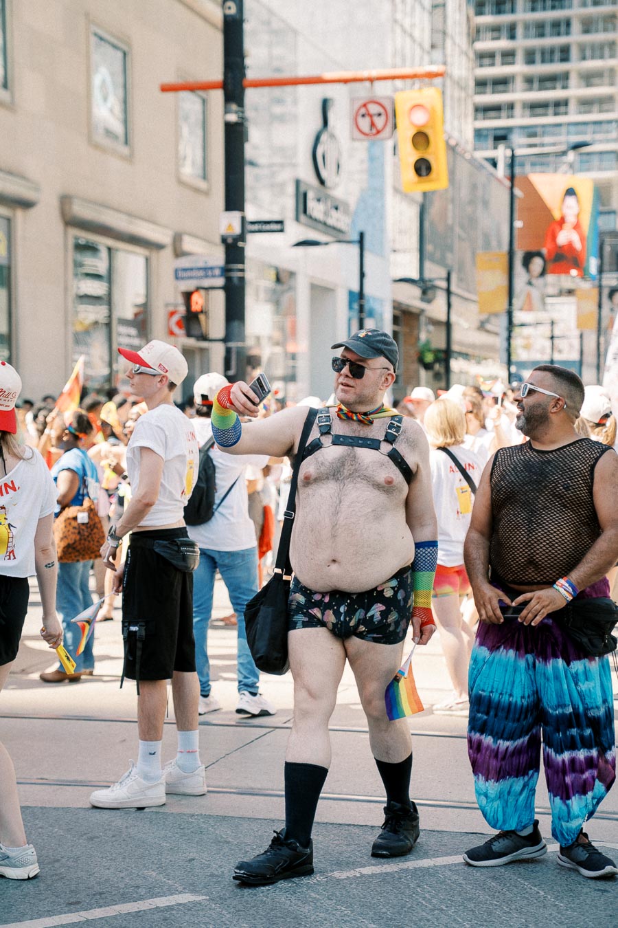 Participants in a pride parade celebrate with colorful attire and rainbow flags, capturing the moment with photos.