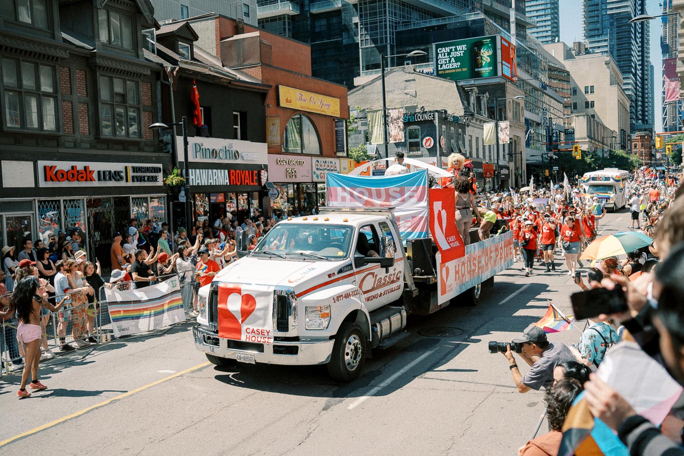 A Casey House float participates in a pride parade in Toronto, with crowds cheering along the street.