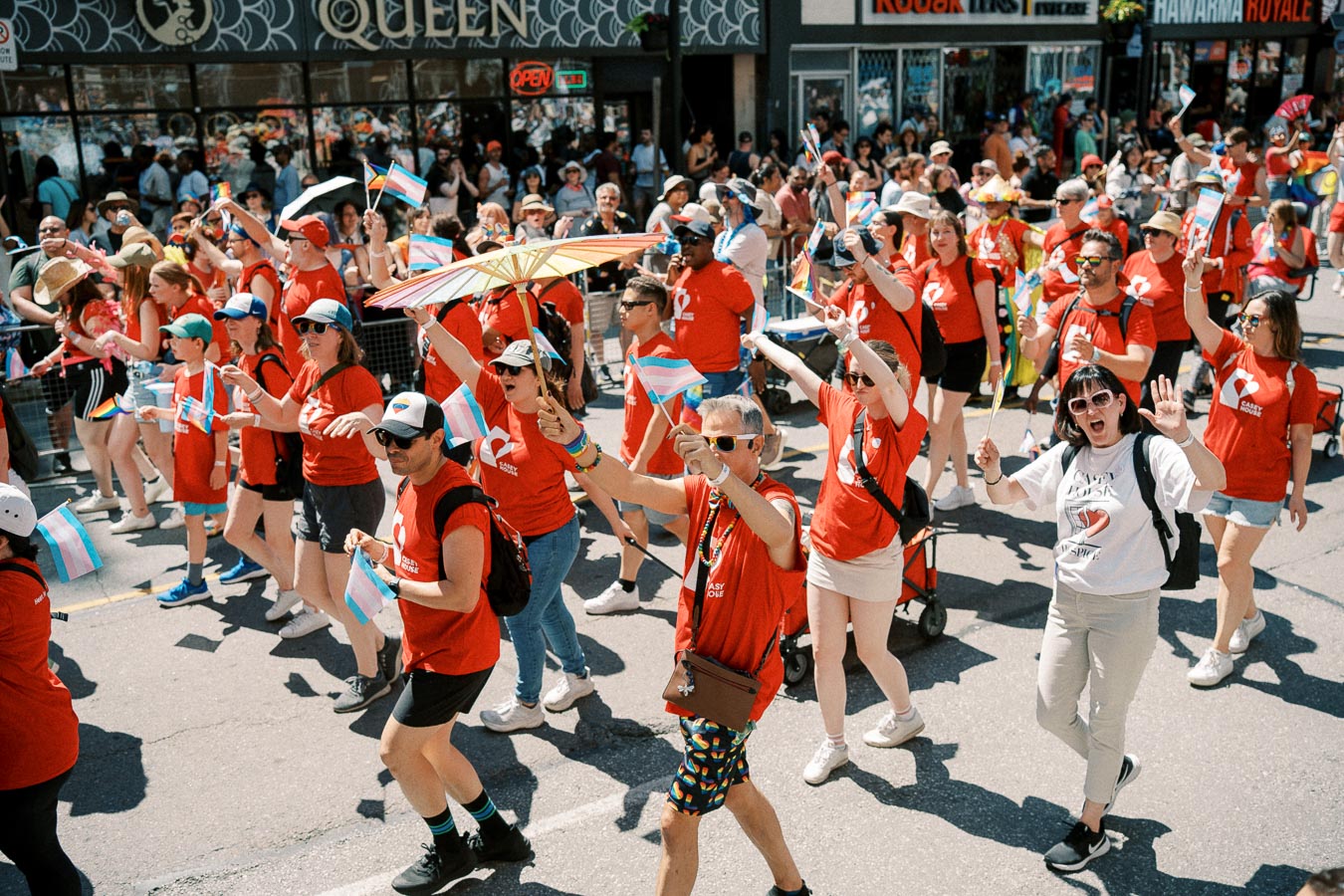 Participants in a parade wearing red shirts and waving flags, with spectators lining the street.