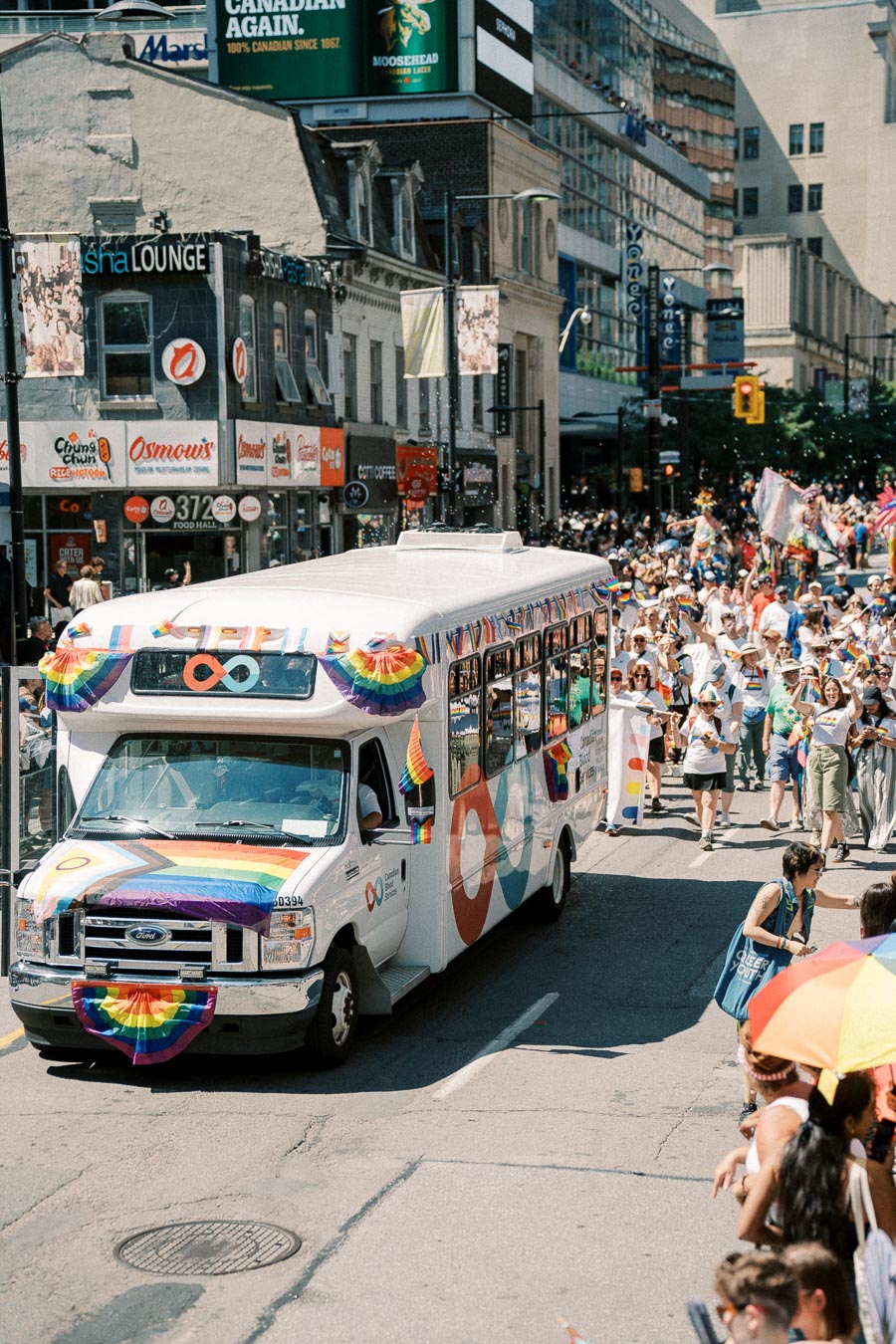 A vibrant parade featuring a decorated bus with rainbow flags, celebrating diversity and inclusion on a bustling city street.