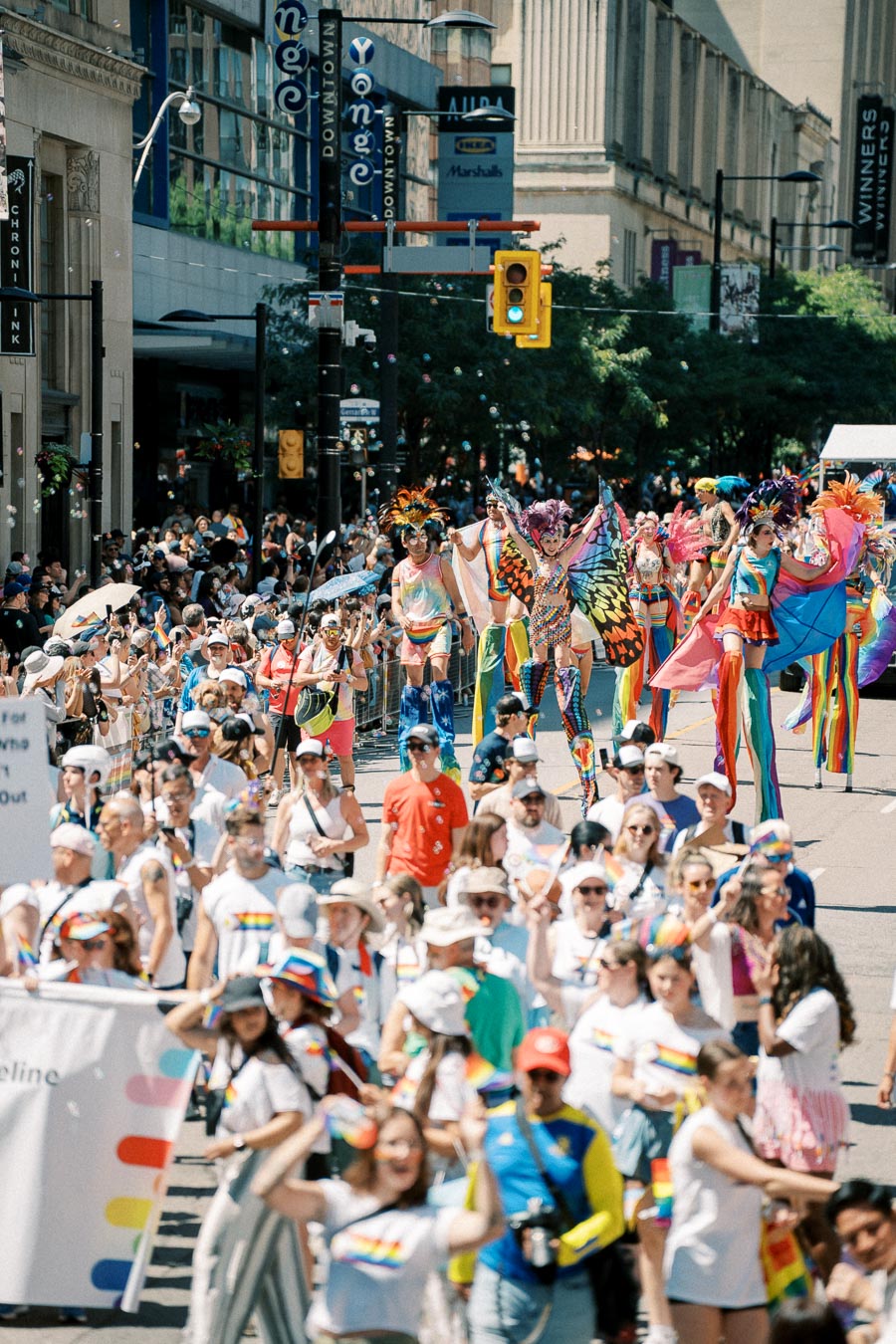 A lively parade featuring participants in colorful costumes and rainbow flags, celebrating diversity on a bustling city street.