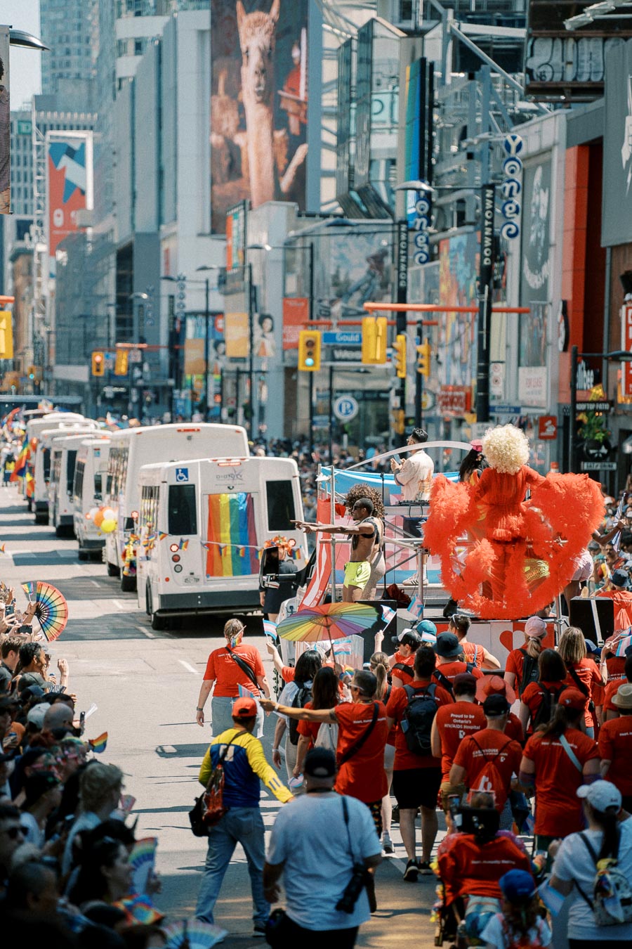 A lively parade featuring colorful floats and participants adorned with rainbow flags moves through a bustling city street, celebrating diversity and inclusion.