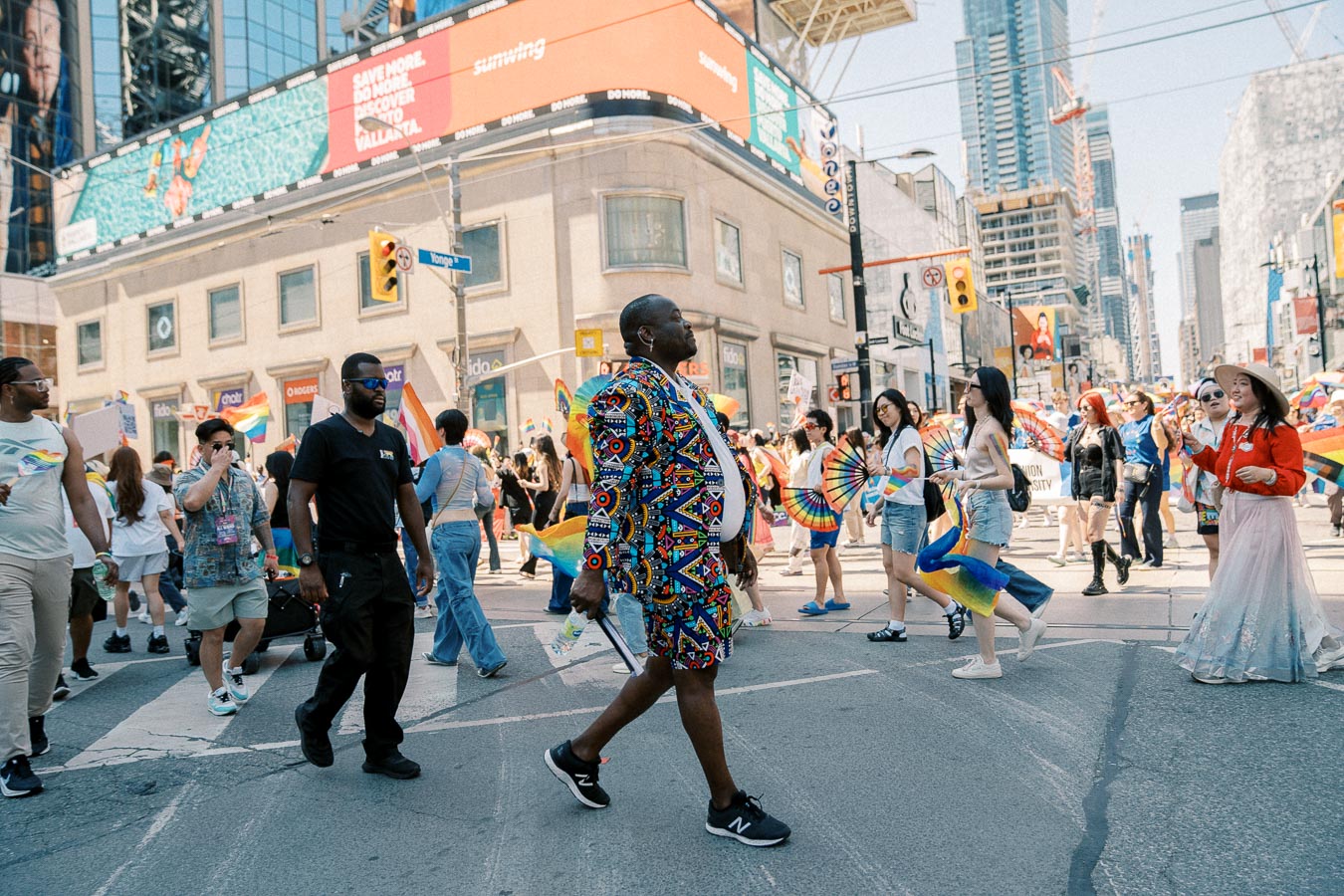 Participants in a vibrant pride parade march through a bustling city street, showcasing colorful outfits and flags.