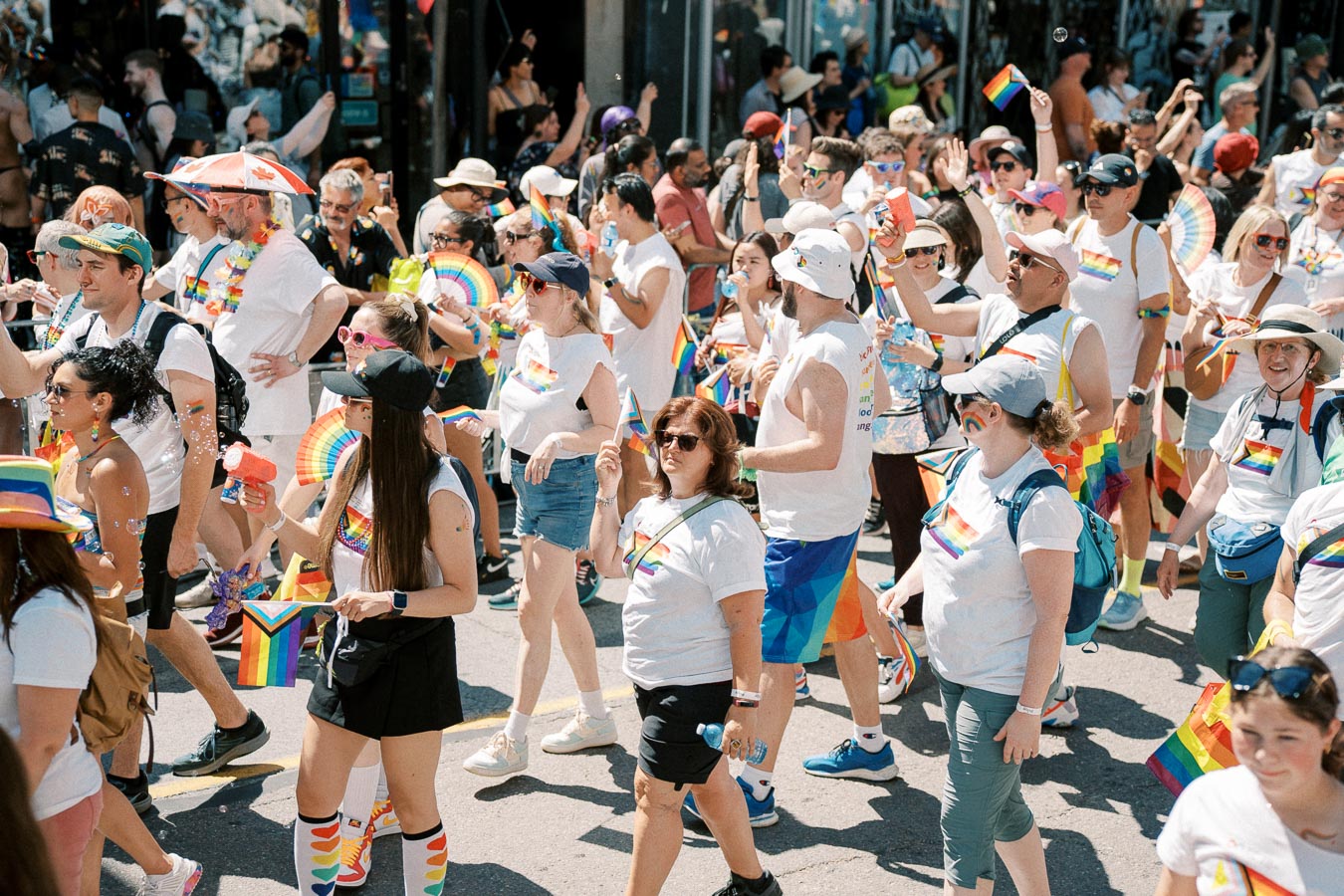 Participants in a pride parade celebrate diversity and inclusion, wearing rainbow-themed attire and carrying flags.