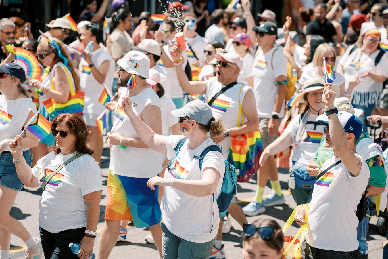 Participants in a pride parade celebrate with rainbow flags and colorful attire, showcasing support for the LGBTQ+ community.