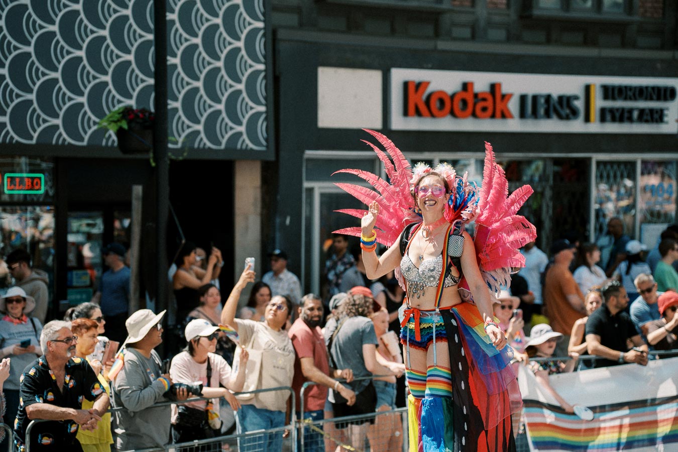 A vibrant parade scene featuring a person in a colorful costume with pink feathers, entertaining a lively crowd.