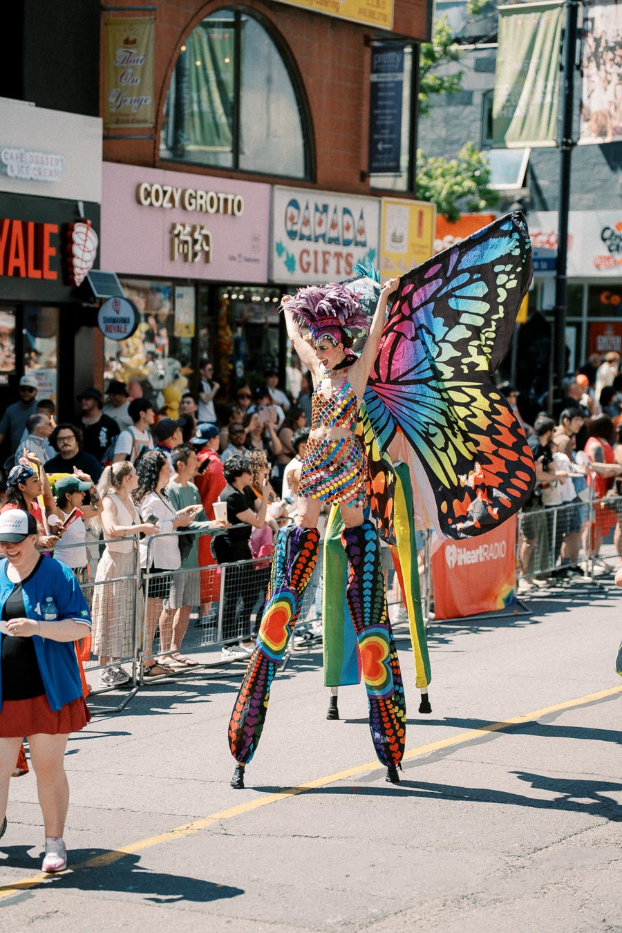 A vibrant performer on stilts dressed as a butterfly entertains the crowd during a lively parade.