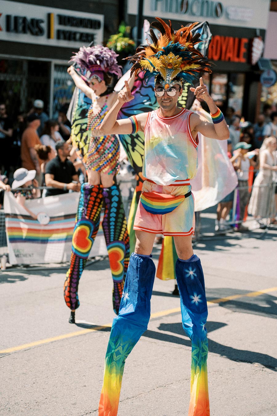 Participants in vibrant costumes and stilts take part in a lively parade, showcasing colorful outfits and feathered headpieces.