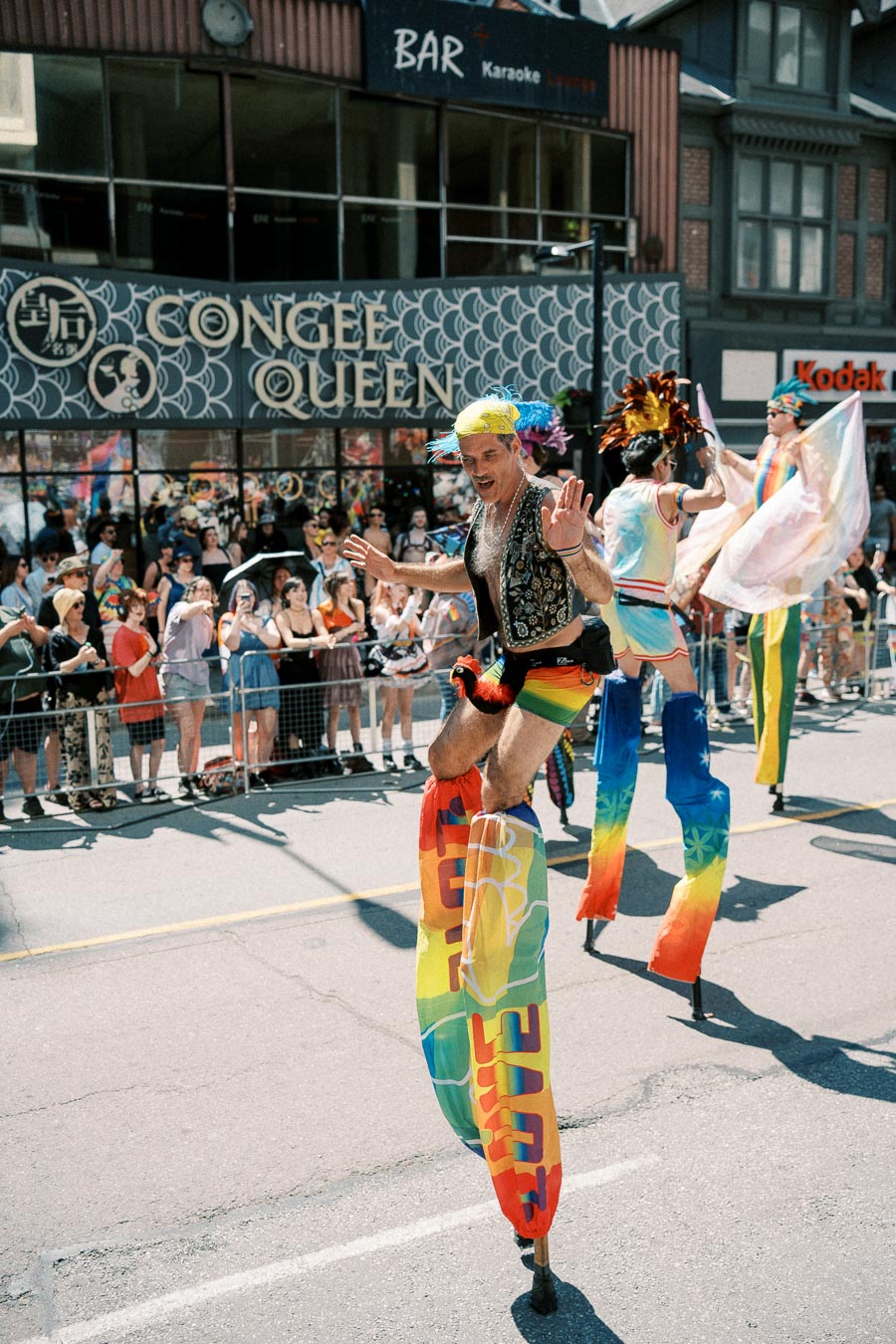 Participants on stilts wearing vibrant rainbow costumes entertain the crowd during a lively parade.