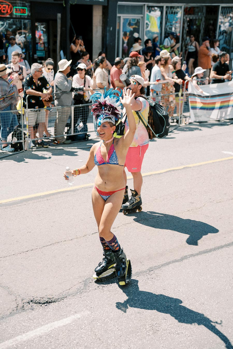 A vibrant parade scene featuring a person in a colorful outfit and feathered headdress roller skating and waving to the crowd.