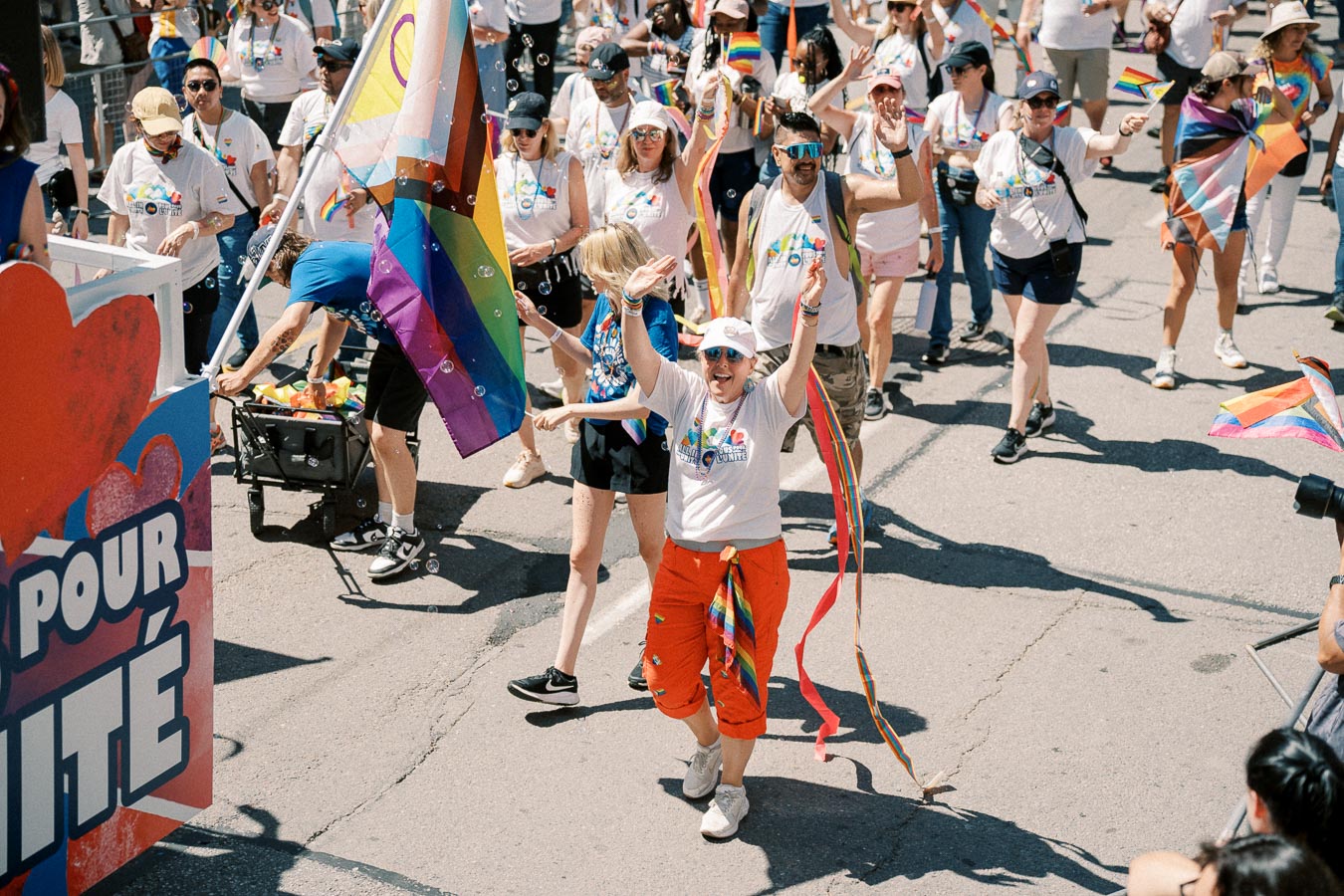 Participants joyfully march in a pride parade, celebrating diversity and inclusion with rainbow flags and vibrant attire.