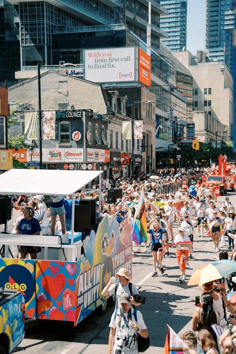 A lively parade celebrating diversity and unity, featuring a colorful float and participants waving rainbow flags, set against an urban backdrop.