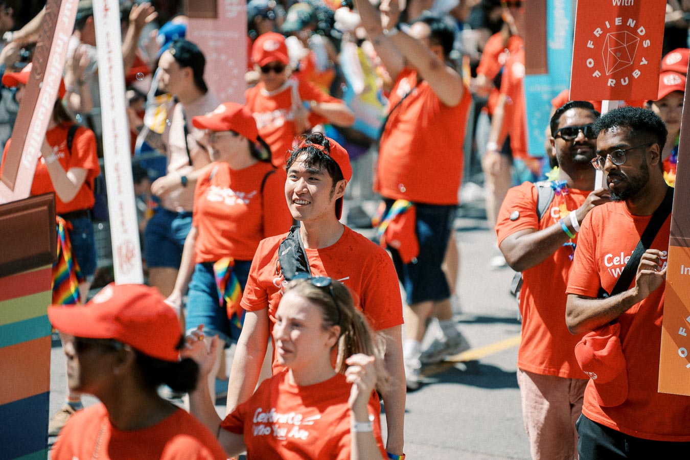 Participants in a parade wearing red shirts and hats, holding signs and celebrating.