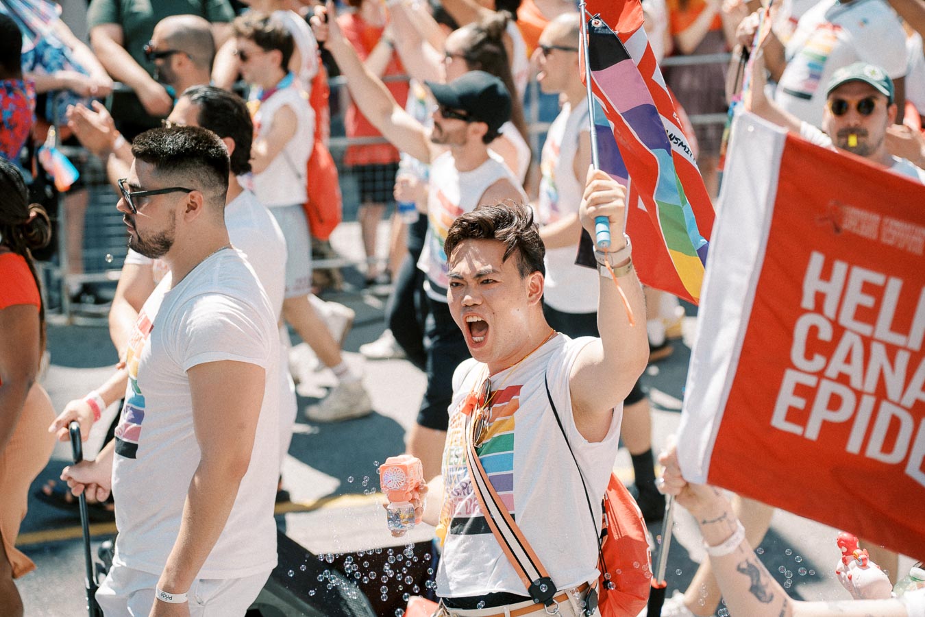 Participants in a pride parade energetically march, waving flags and wearing rainbow-themed attire.