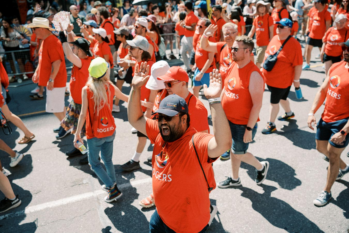 Participants in a parade wearing red Rogers shirts walk down the street, celebrating with raised hands.