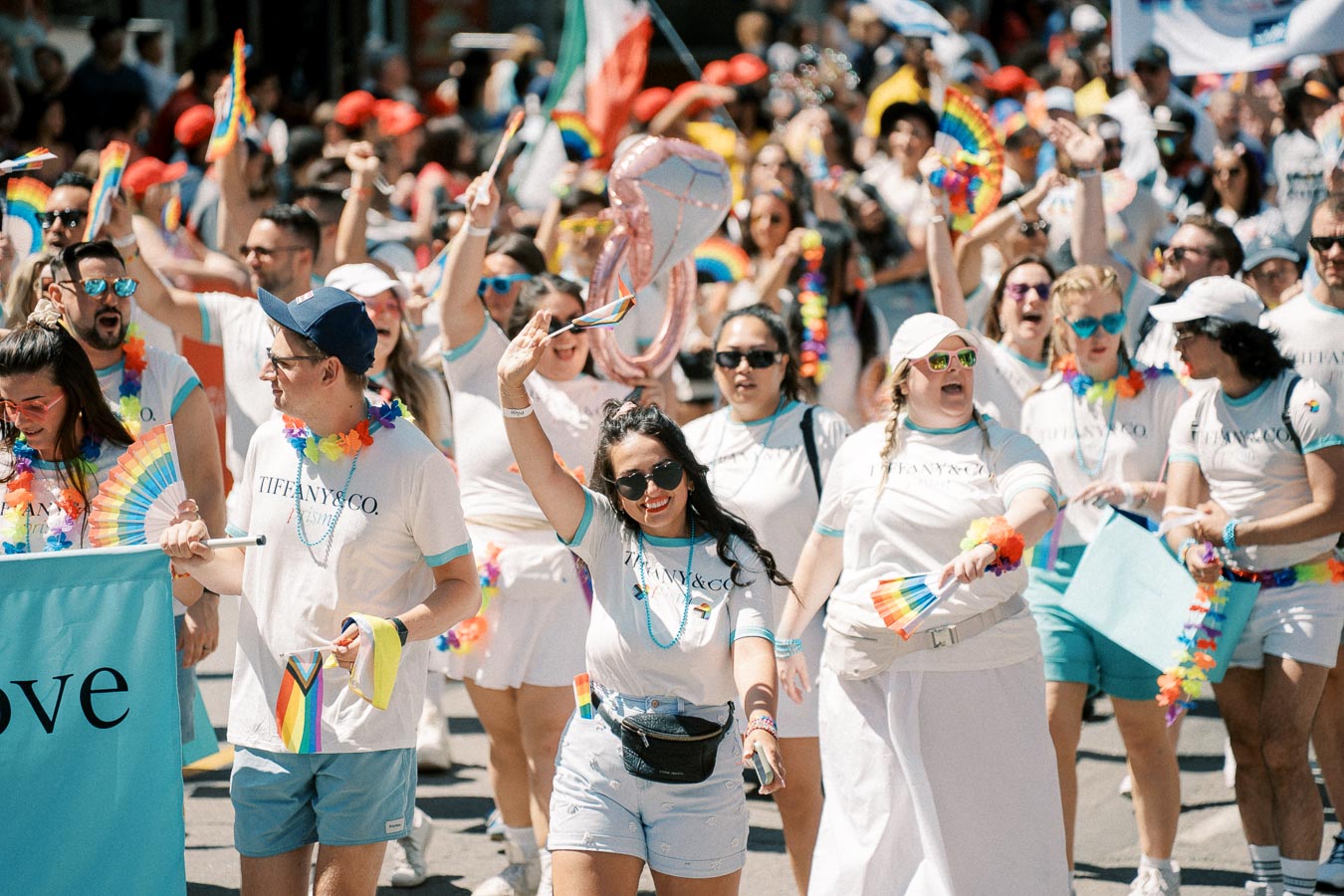 Participants at a pride parade joyfully march with rainbow flags and accessories, celebrating diversity and inclusion.