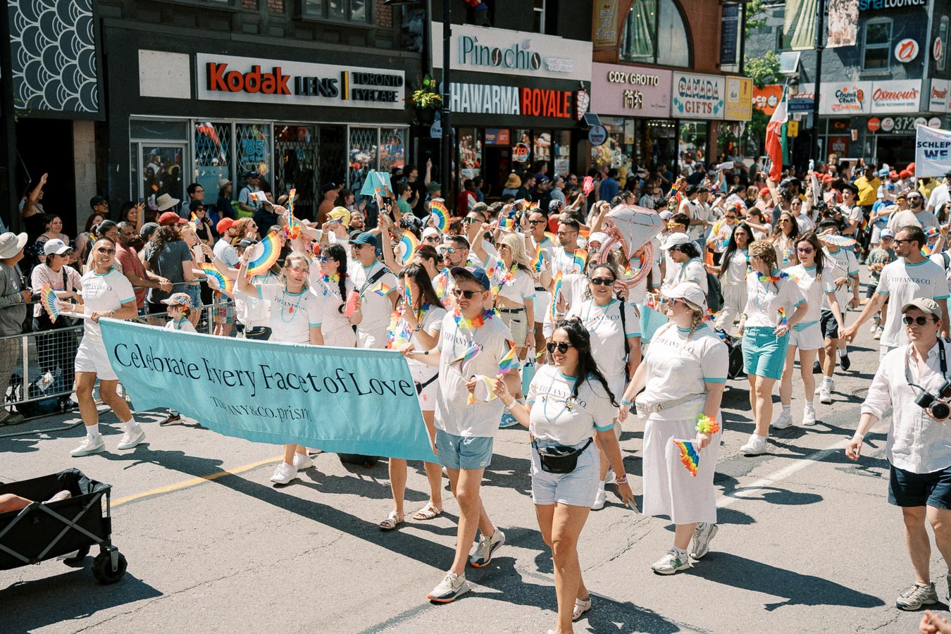 Participants in a pride parade march with a banner reading 'Celebrate Every Facet of Love', showcasing support for LGBTQ+ rights.