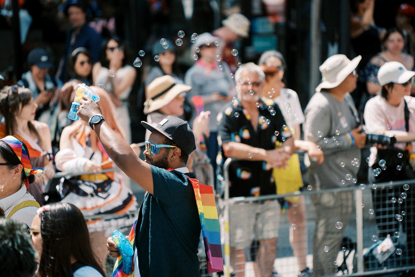 A lively scene at a pride parade with a person blowing bubbles, surrounded by a diverse crowd.