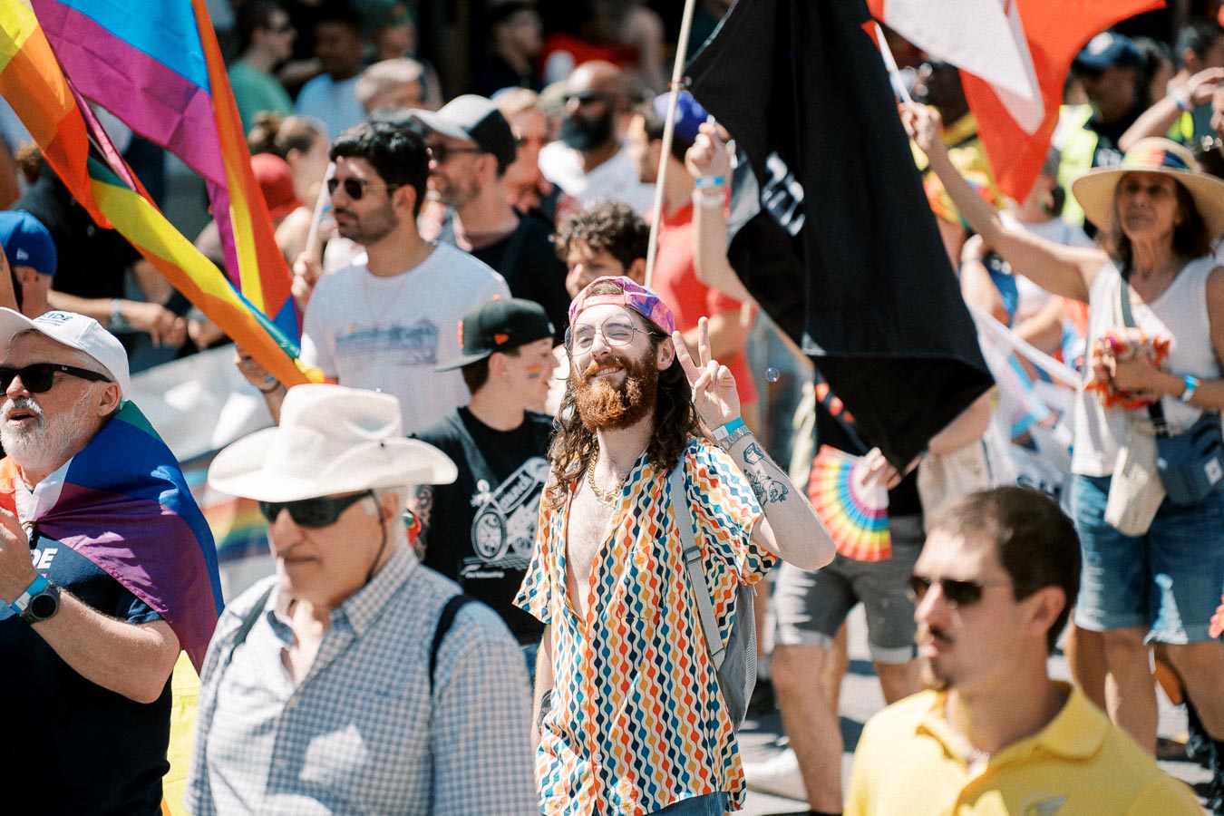 Participants celebrate at a pride parade, showcasing vibrant attire and flags.