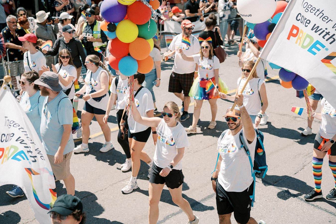Participants in a Pride parade celebrate with colorful balloons and flags, wearing themed attire to show support for the LGBTQ+ community.
