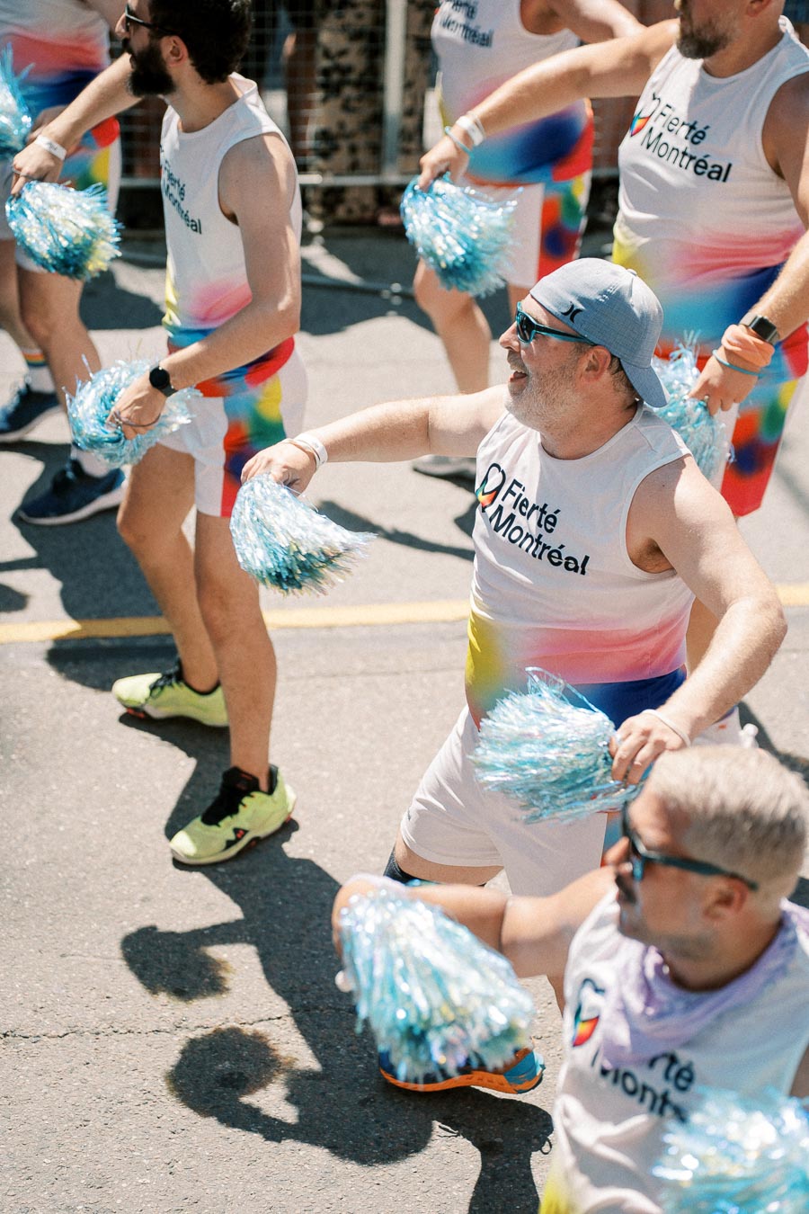 Participants in the Fierté Montréal parade cheerfully march with colorful outfits and pom-poms.