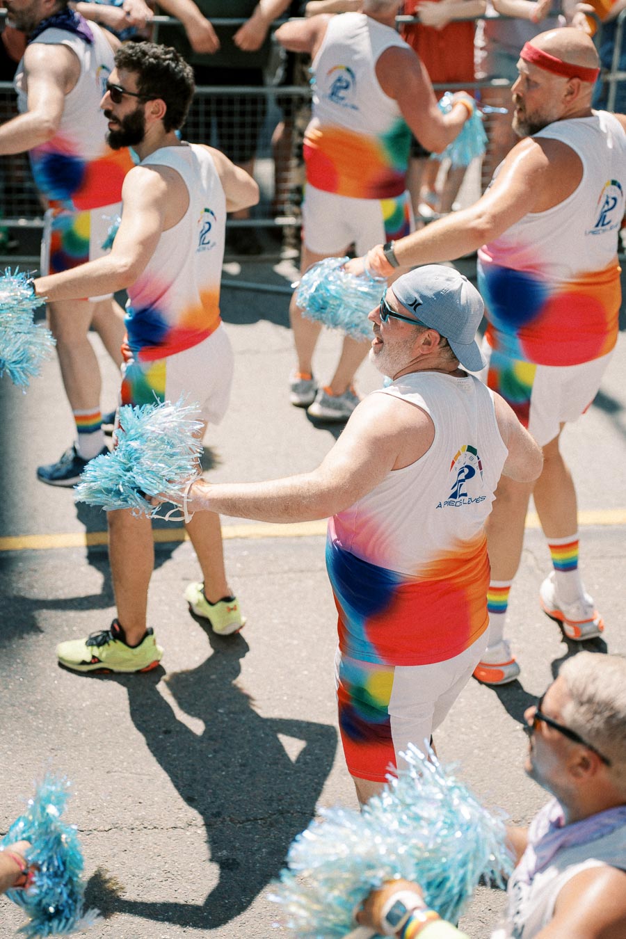 Participants in a parade wearing colorful outfits and holding blue pom-poms, celebrating with enthusiasm.
