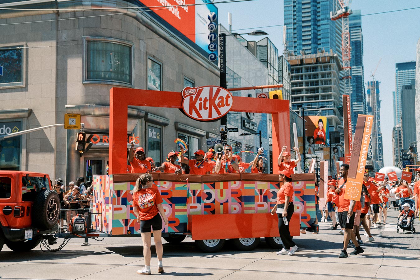 A KitKat-themed float participates in a city parade, with people in red shirts celebrating and holding signs.