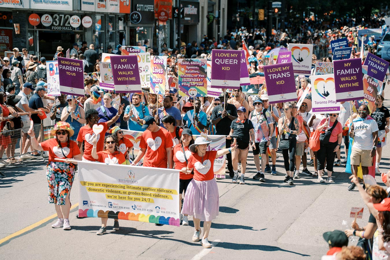 Participants in a pride parade march with signs promoting LGBTQ+ rights and family support, showcasing messages of love and acceptance.