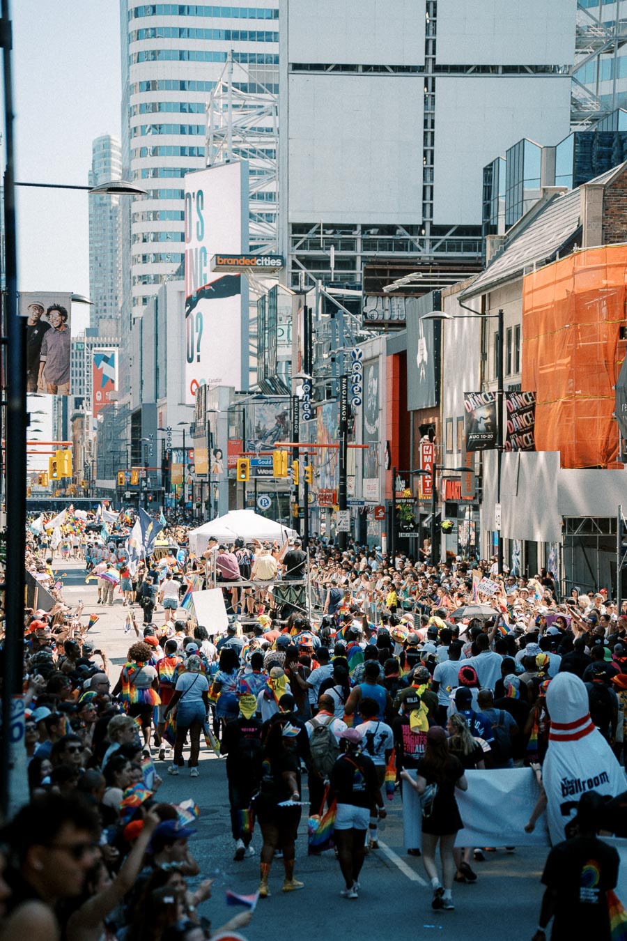A lively parade takes place in a bustling city street, with participants and spectators celebrating amidst tall buildings and vibrant decorations.