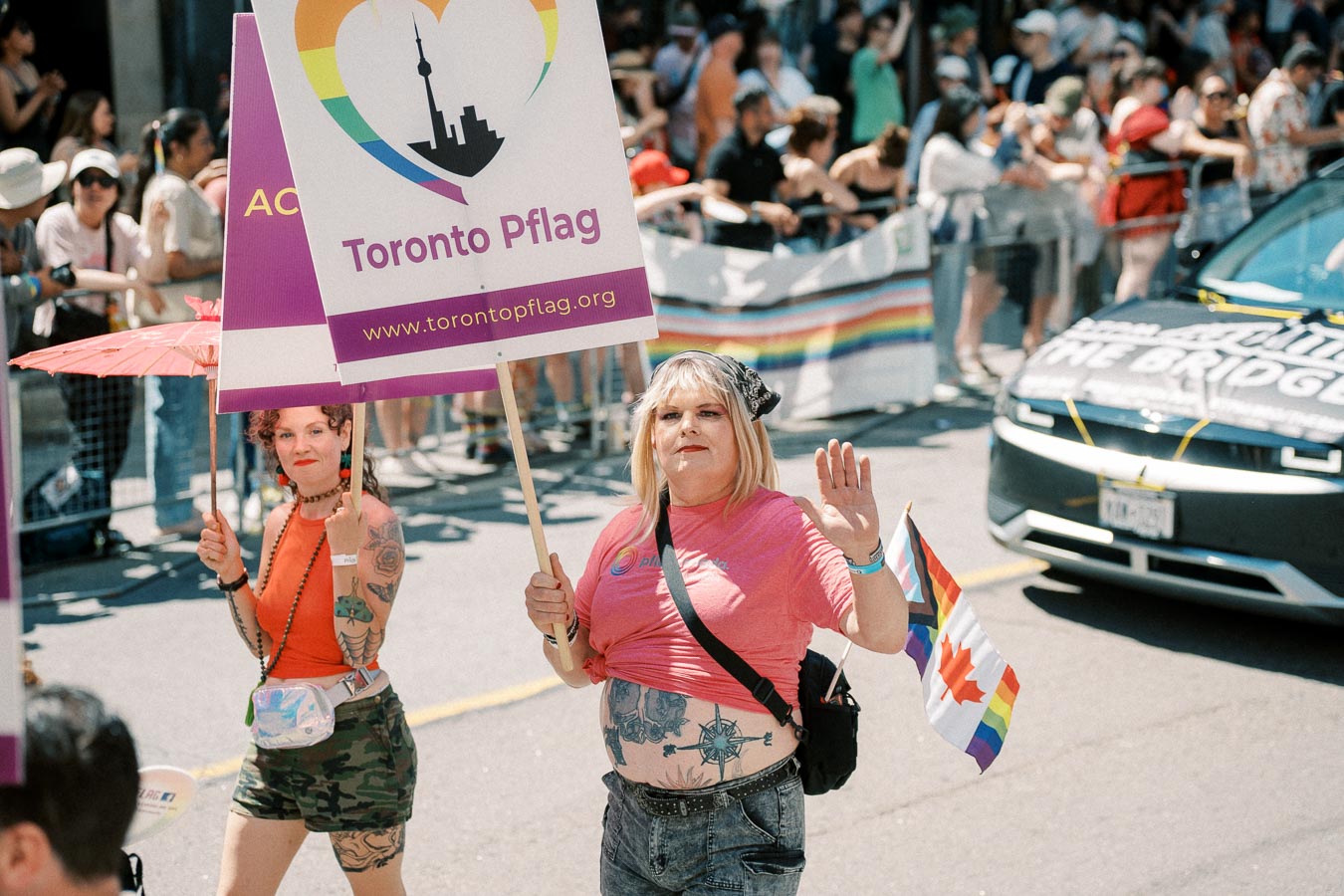 Participants in a pride parade hold a Toronto Pflag sign and a rainbow flag, celebrating diversity and inclusion.