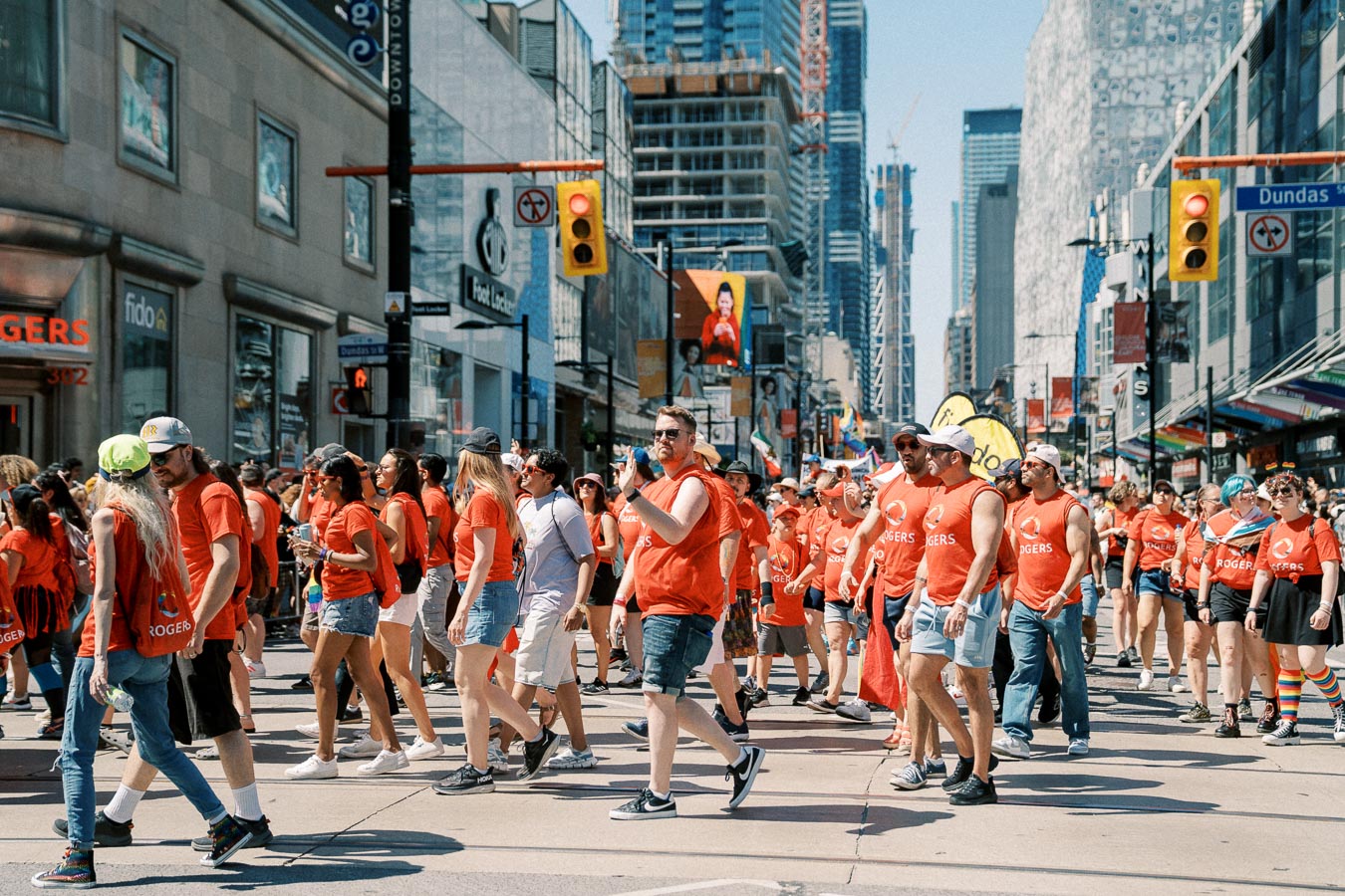 A crowd of people wearing red shirts participates in a parade on a city street, with buildings and construction visible in the background.