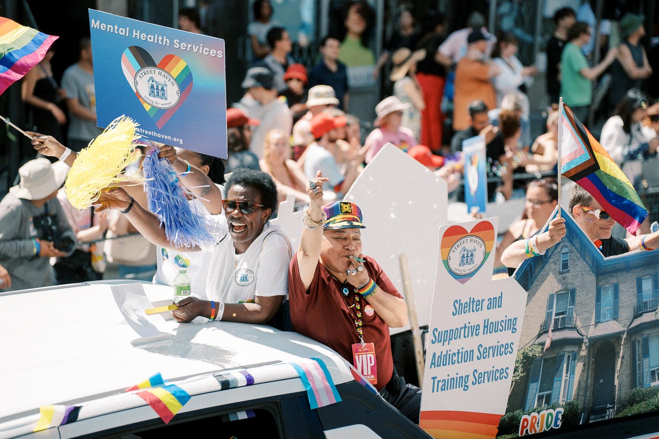 Participants in a Pride parade celebrate with signs promoting mental health services and supportive housing.