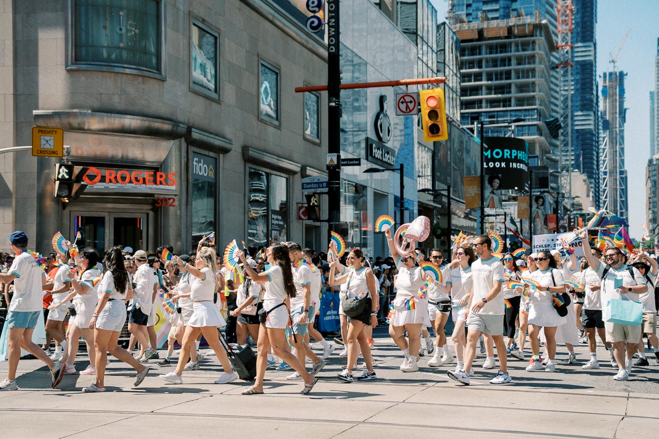 Participants in a pride parade march through a city street, celebrating with rainbow-themed accessories and decorations.