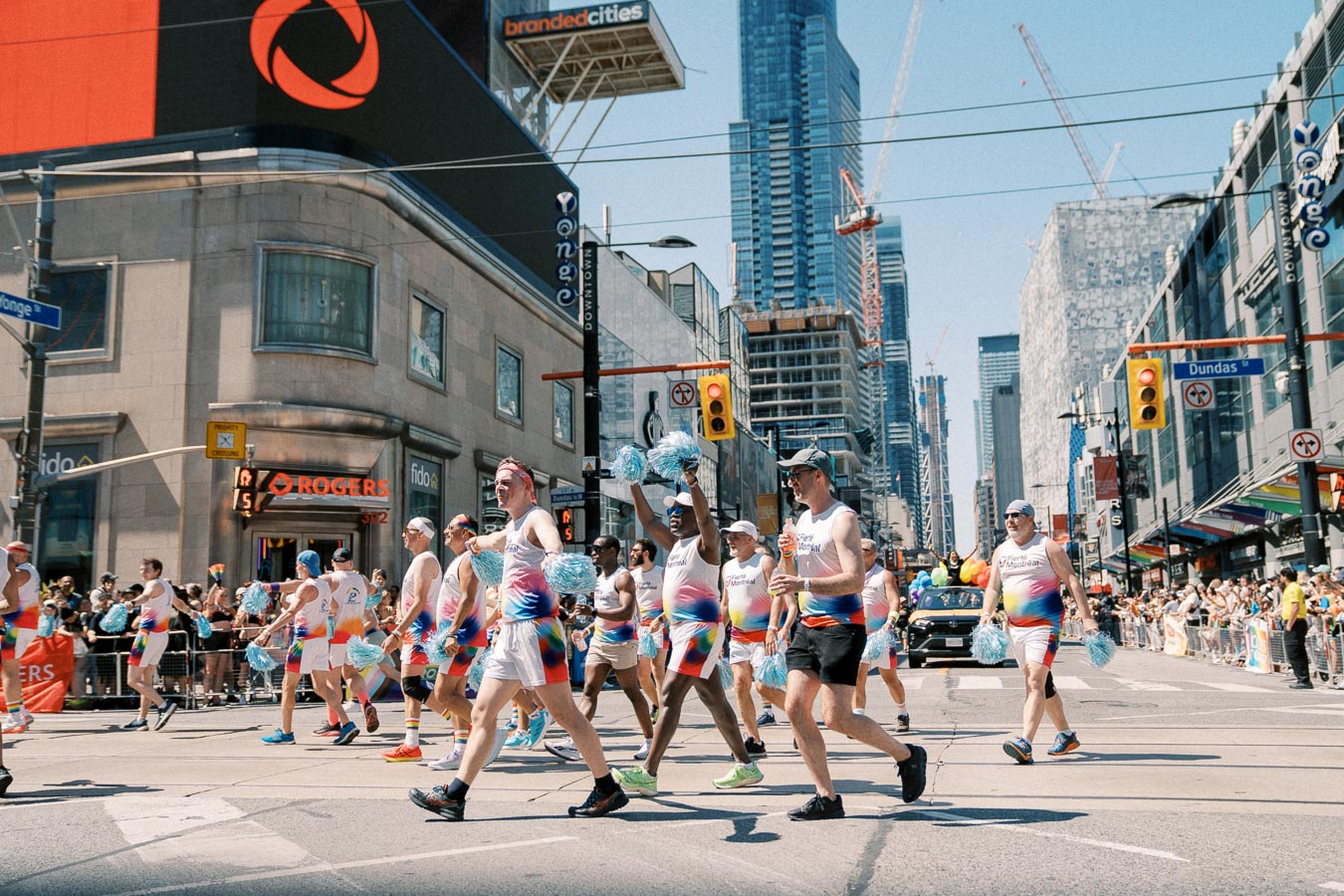 Participants in colorful outfits march in a parade on Yonge Street, Toronto, during a sunny day, with spectators lining the street.