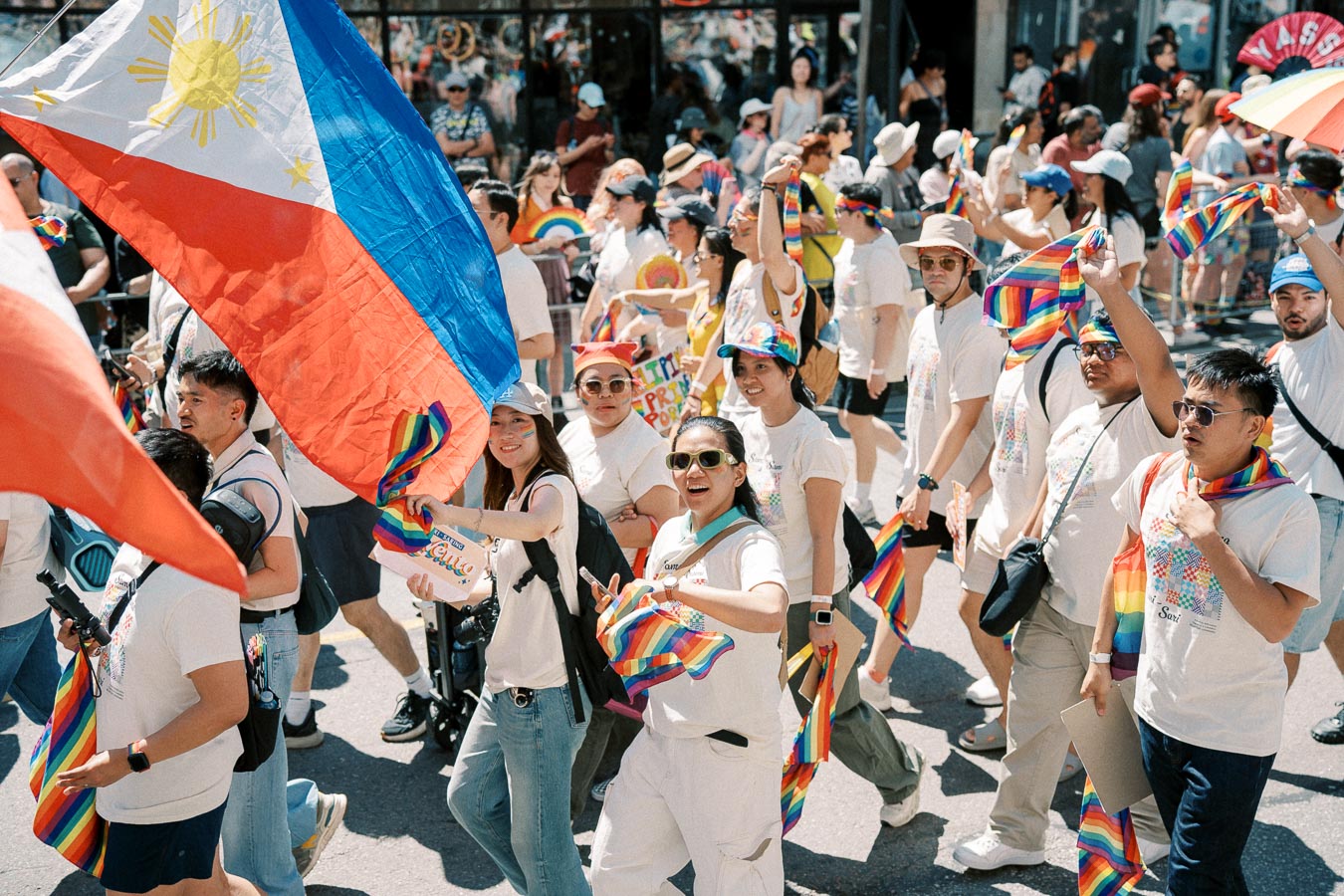 Participants in a parade celebrate with rainbow flags and a large Philippine flag, showcasing diversity and pride.