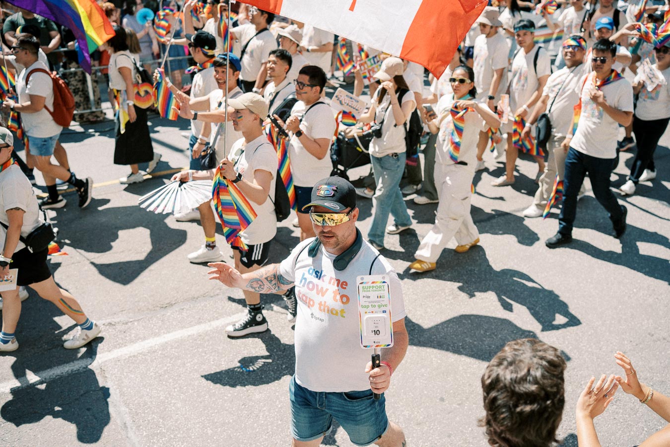 Participants in a pride parade march down the street, waving rainbow flags and wearing colorful outfits, celebrating diversity and inclusion.
